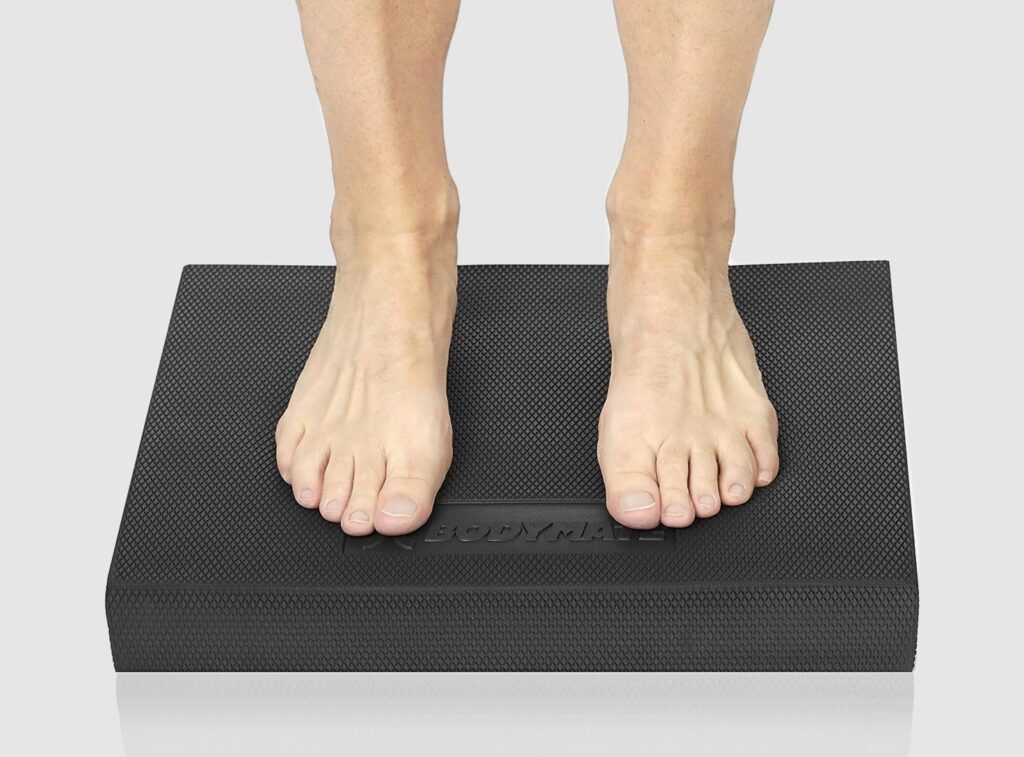 Hände halten BODYMATE Balance Pad Schwarz grauer Hintergrund