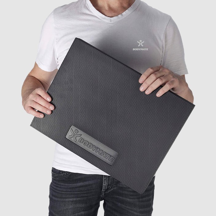 Mann weißes T-Shirt hält BODYMATE Balance Pad schwarz grauer Hintergrund